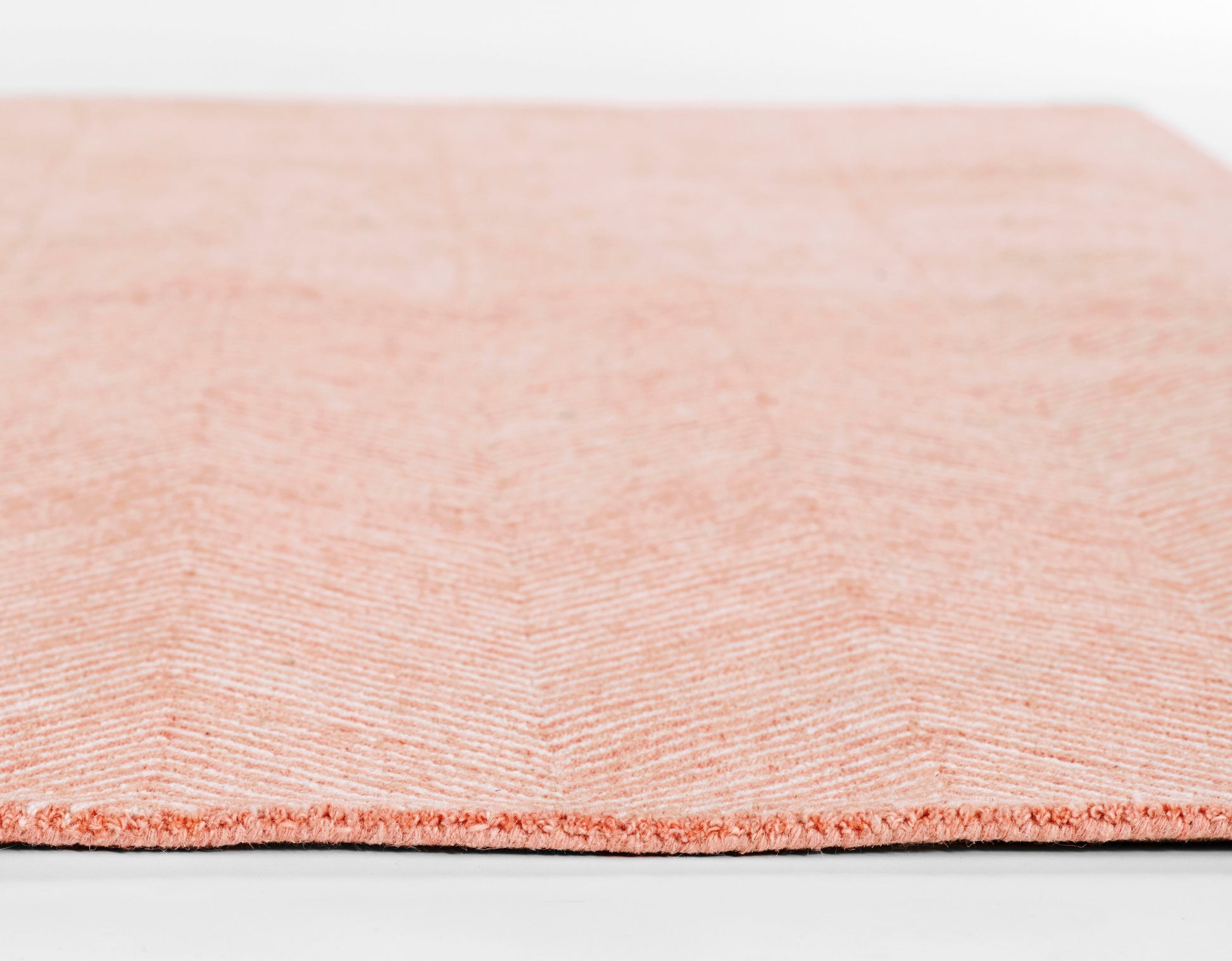 Peach-pink chevron-patterned rug with plush pile and stitched edge, close-up texture.