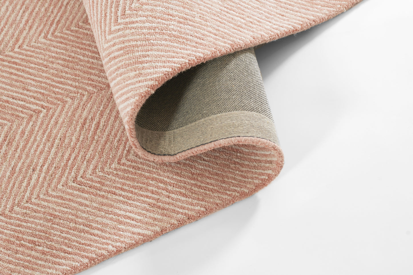 Pink textured rug with chevron ribbed pattern and soft pile; folded corner reveals grey non-slip backing.