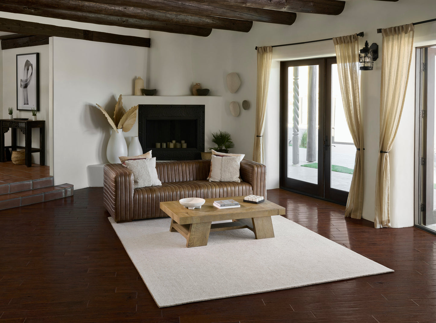 Rustic living room with brown leather sofa, chunky wood coffee table, cream rug, fireplace, beige curtains.