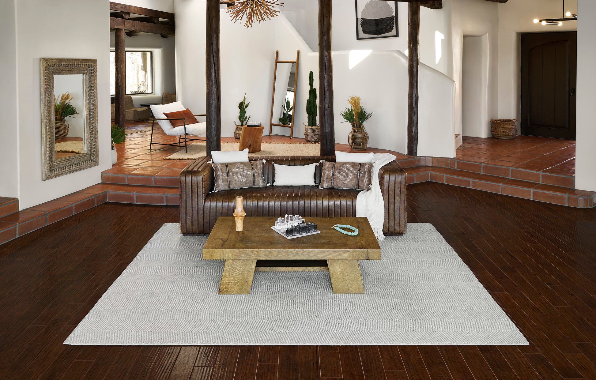 Taupe tufted leather sofa, rustic wood coffee table, light gray rug, dark wood floors, terracotta steps, potted plants.
