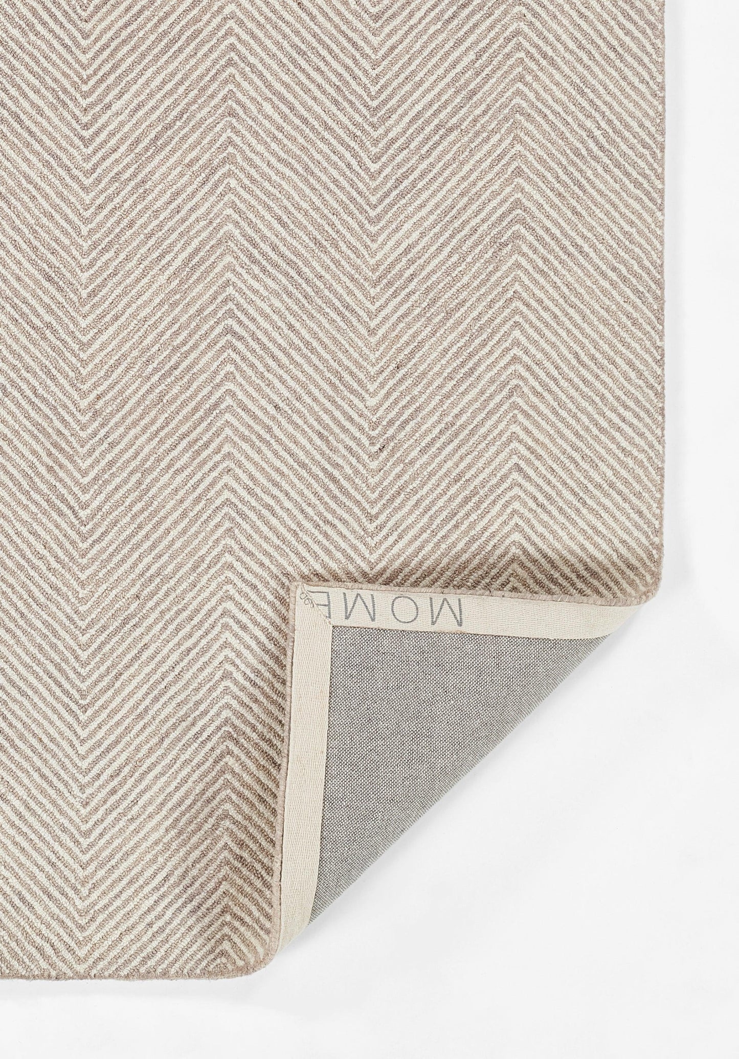 Taupe chevron herringbone rug with woven texture; corner folded to show gray backing and beige binding.