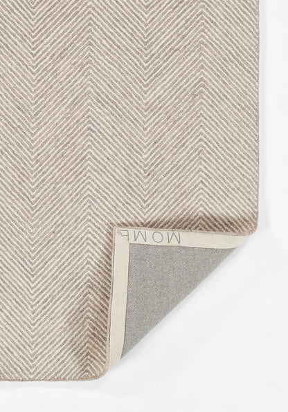 Taupe herringbone throw blanket, folded at corner to reveal grey reverse side and cream binding.