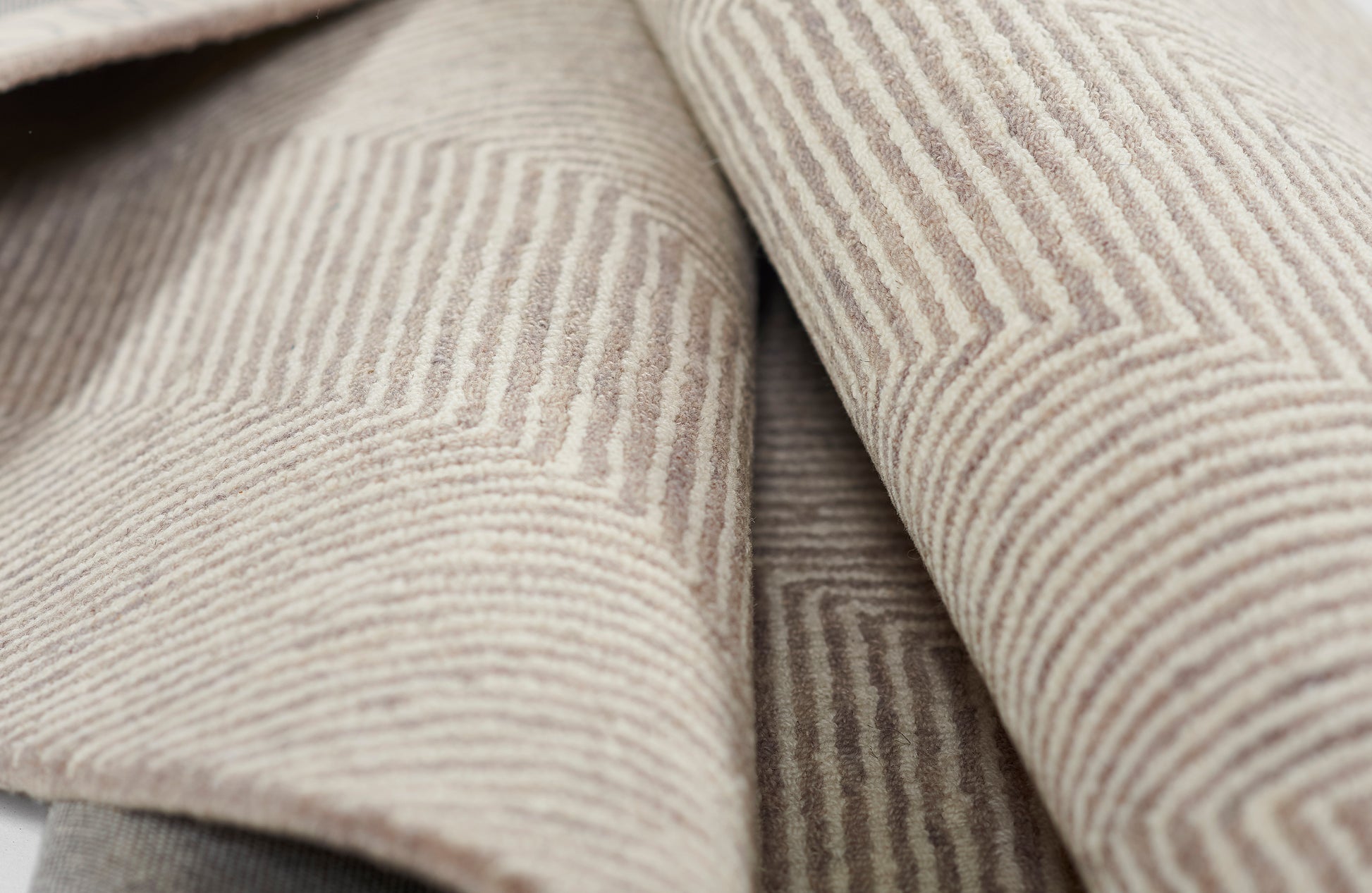 Taupe corduroy fabric close-up with narrow beige wales & soft textured folds, ideal for jackets or upholstery.