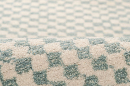 Macro view of a light blue and ivory checkerboard plush rug with soft, high-pile texture.