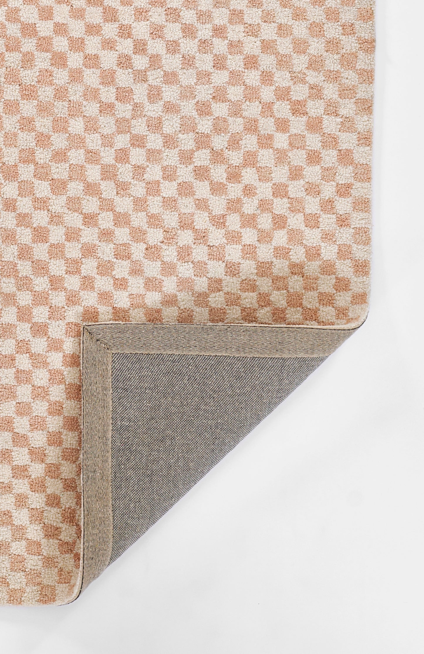 Peach and cream checker-textured rug with beige edge; corner folded to reveal grey fabric underside.