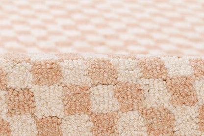 Soft plush rug with peach and cream checker blocks; thick loop-pile texture.