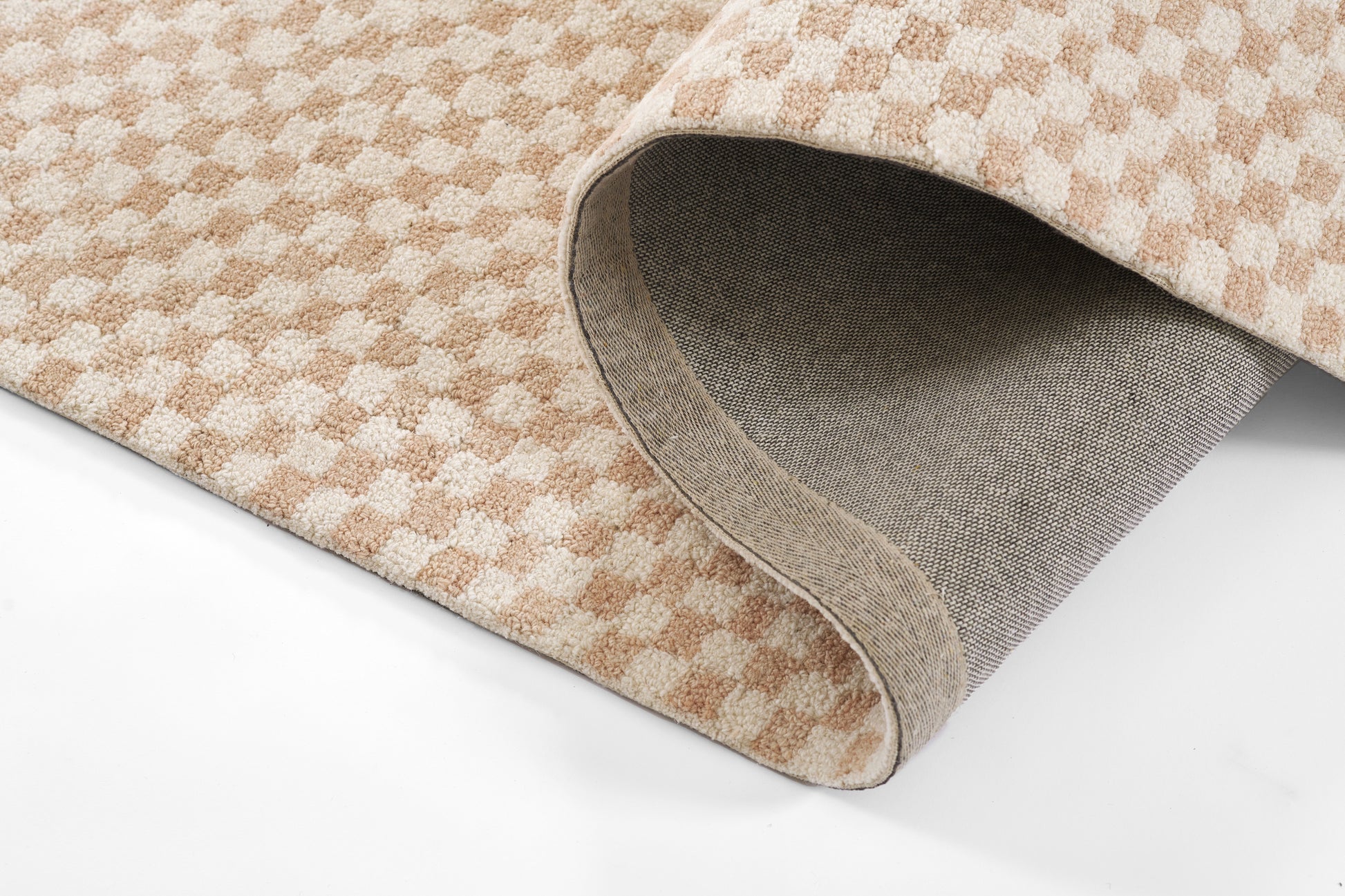 Beige-pink checkered rug with soft loop pile; rolled edge shows grey woven backing.