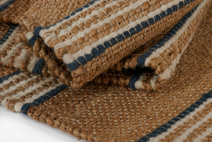 Handwoven jute rug in natural brown with navy blue and cream stripes; chunky textured weave, rustic coastal style.