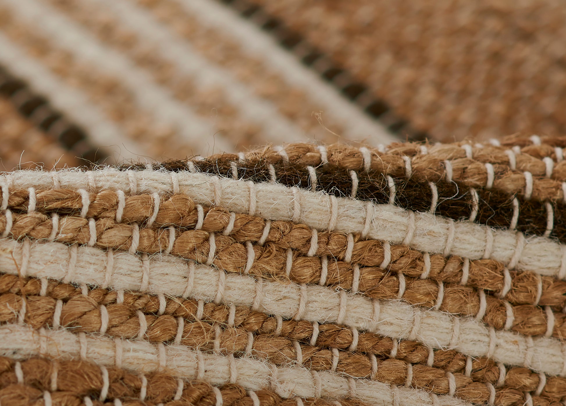 Close-up of a natural brown and cream striped woven rug with chunky jute fibers and white stitching.