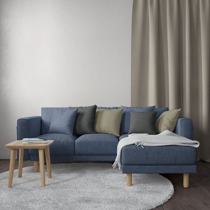 Blue solid fabric sectional with chaise, light wood legs, blue/gray/olive cushions, cream throw, small wood coffee table, gray rug.