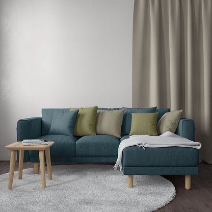 Teal solid fabric upholstery on an L-shaped sofa with light wood legs, olive and beige cushions, gray throw, round side table, beige curtains.