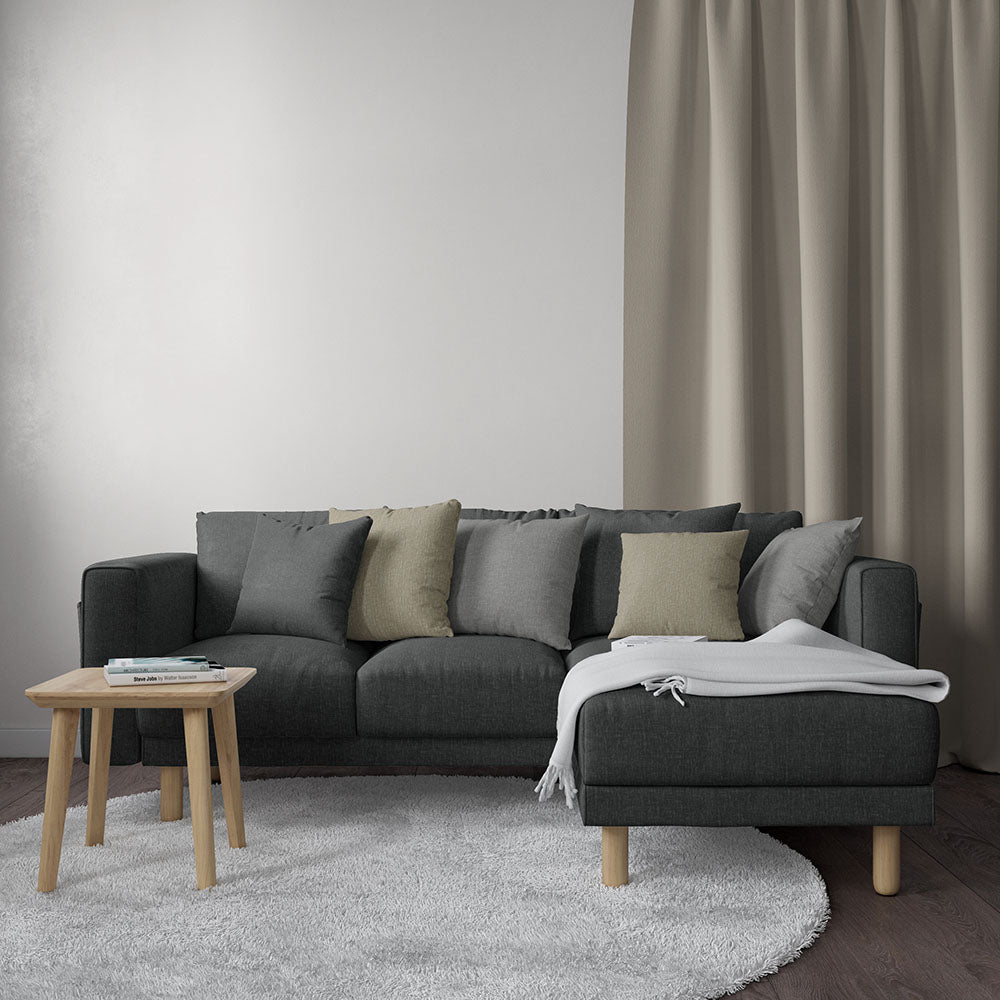 Charcoal solid fabric sofa with a right chaise, beige/gray cushions, light wood legs, white throw—modern living room setup.