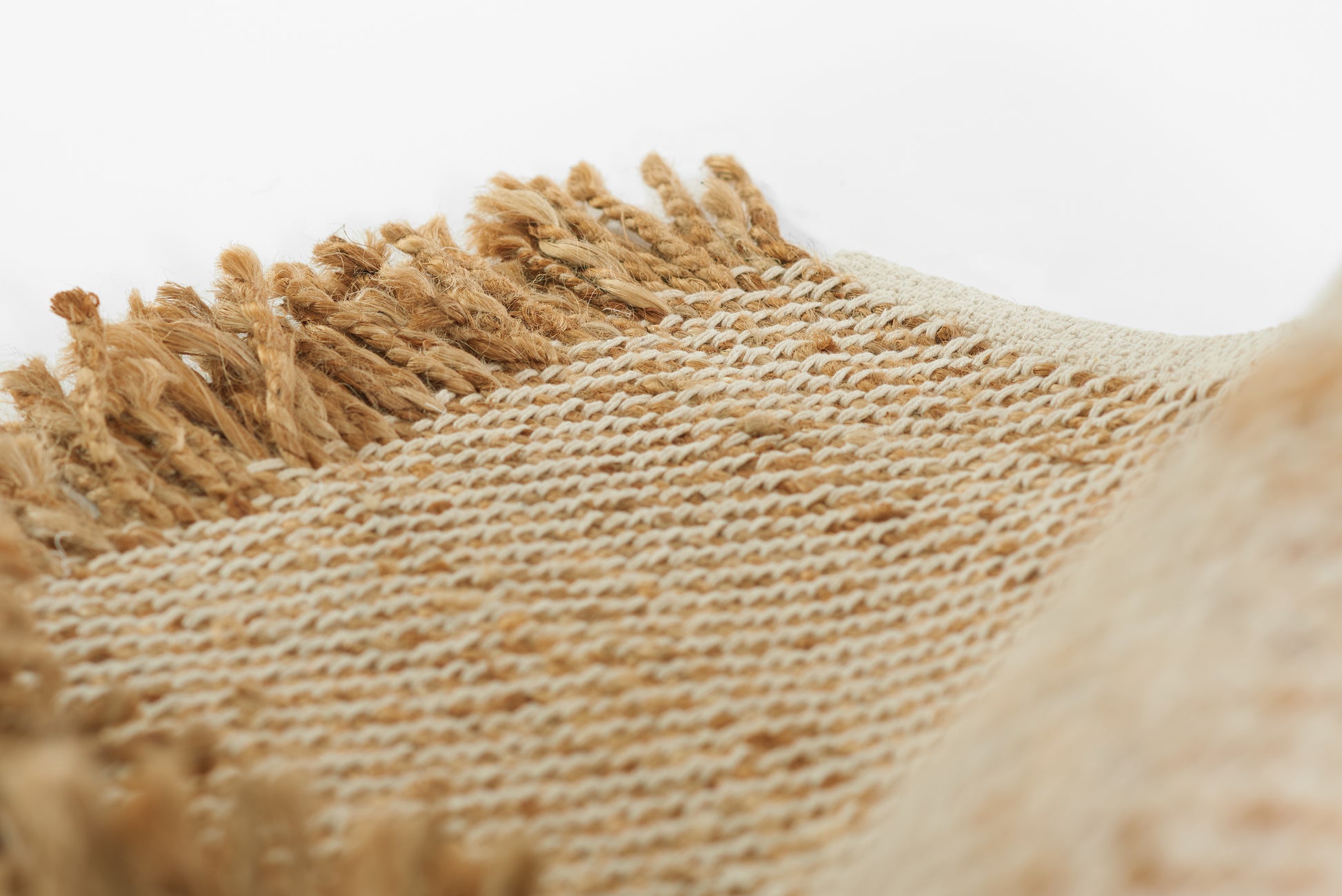 Natural beige woven rug with fringe along the edges, rustic jute-like fabric.