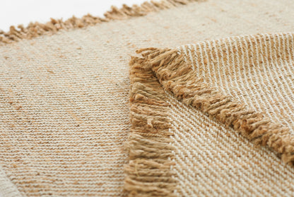 Natural beige jute rug with fringed edges, close-up woven texture, rustic coastal style.