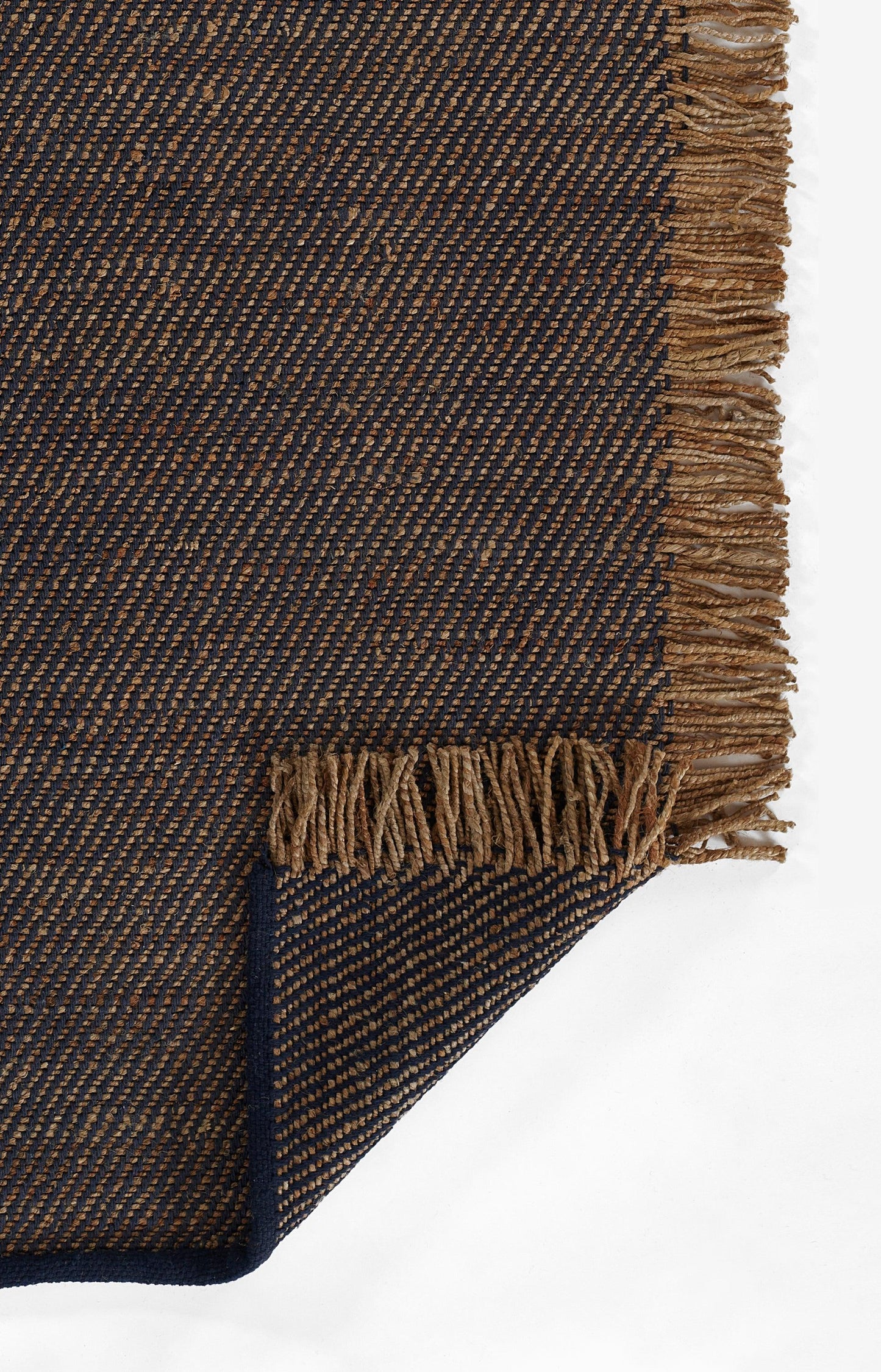 Dark navy and tan woven rug with diagonal stripes, brown fringe along edges; corner folded.