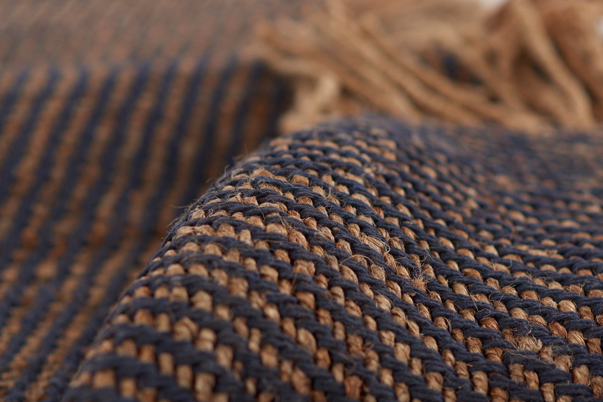 Close-up of navy blue & natural tan woven jute rug with braided texture, rustic boho floor mat.