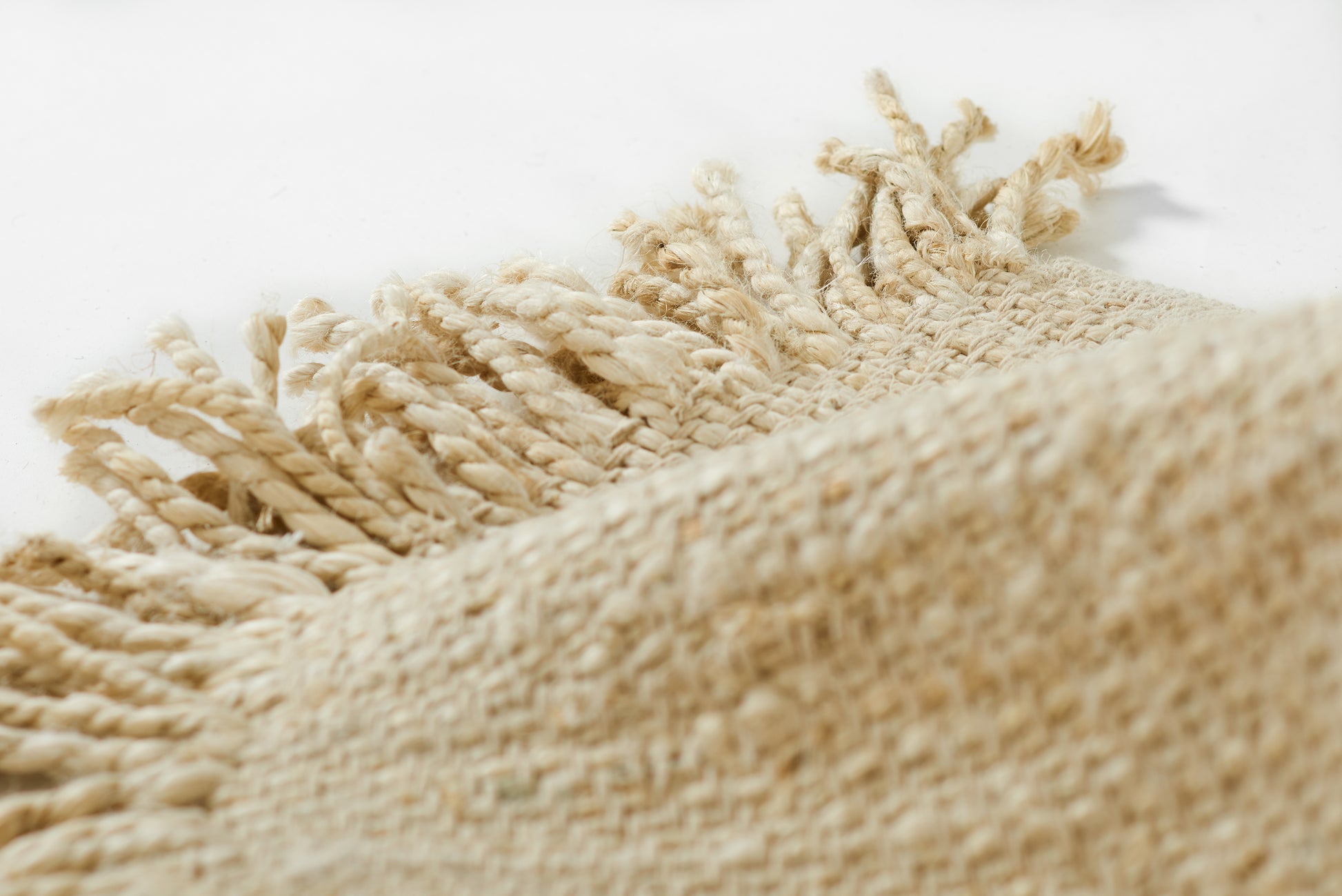 Beige woven jute rug with knotted fringe along the edge, natural fiber texture.