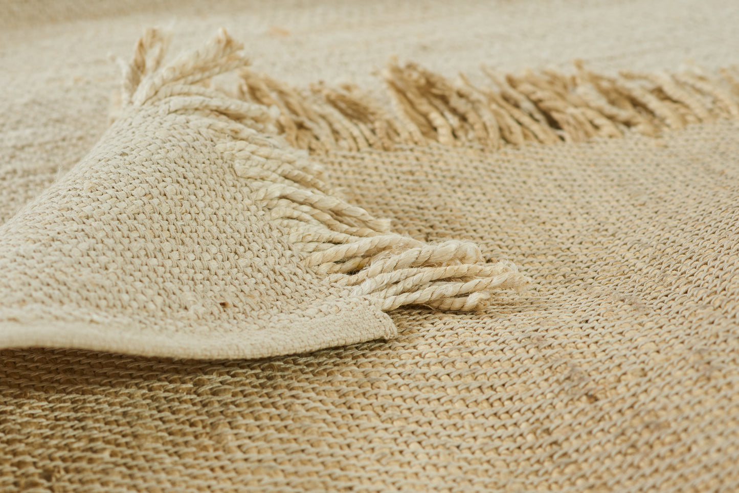 Beige woven jute rug with natural texture and twisted fringe along the edge.