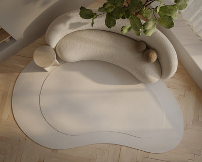Ivory curved modular sofa with soft fabric and pebble cushions, placed on a circular beige rug in a sunlit room.