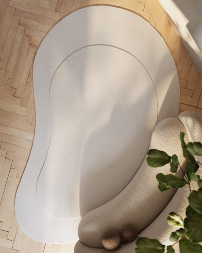 Cream rectangular rug with plush texture on light wood floor; organic curved design, near a plant.