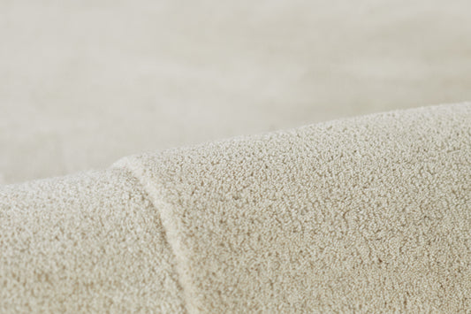 Cream boucle rug close-up showing soft loop pile and rolled edge.