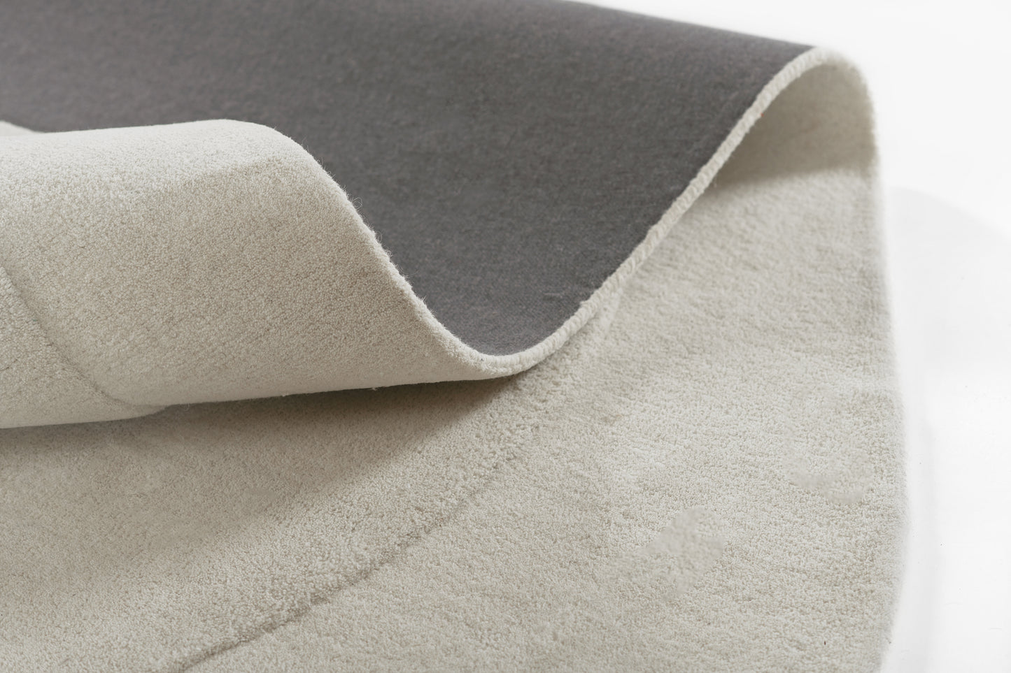 Two-tone felt rug with dark gray top and light beige underside, folded to show soft texture.