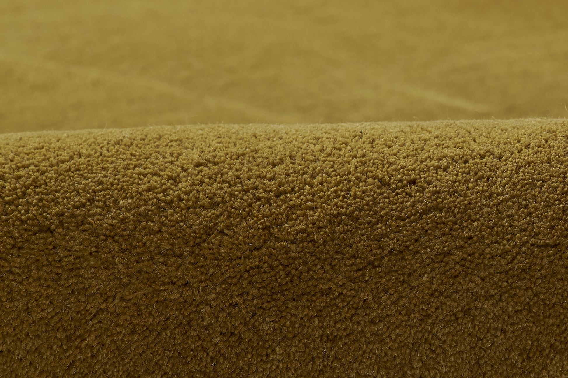 Close-up of warm caramel-brown boucle rug texture with tiny looped fibers and a curved edge.