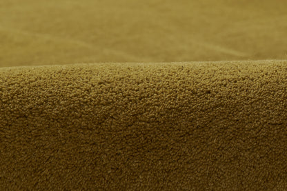 Close-up of warm caramel-brown boucle rug texture with tiny looped fibers and a curved edge.