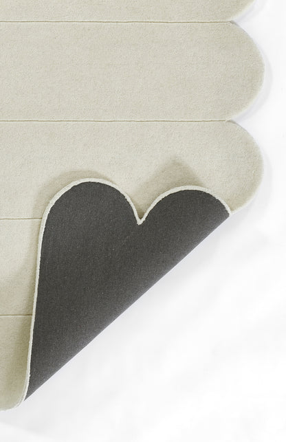 Beige rug with scalloped rounded corner edges, folded to reveal a dark gray underside.