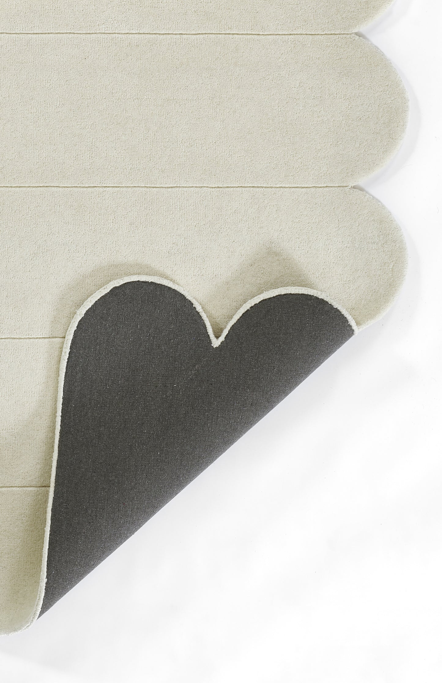Beige layered rug with scalloped rounded edge curling to reveal dark gray underside.