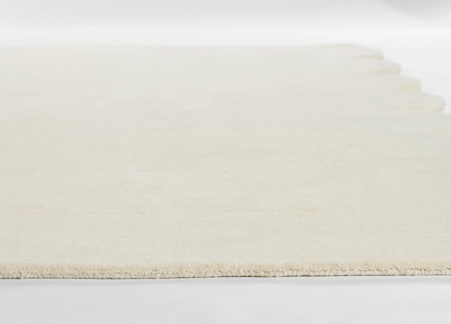 Cream rug with scalloped fringe along one edge; soft, low-pile texture, rectangular coastal-style decor.