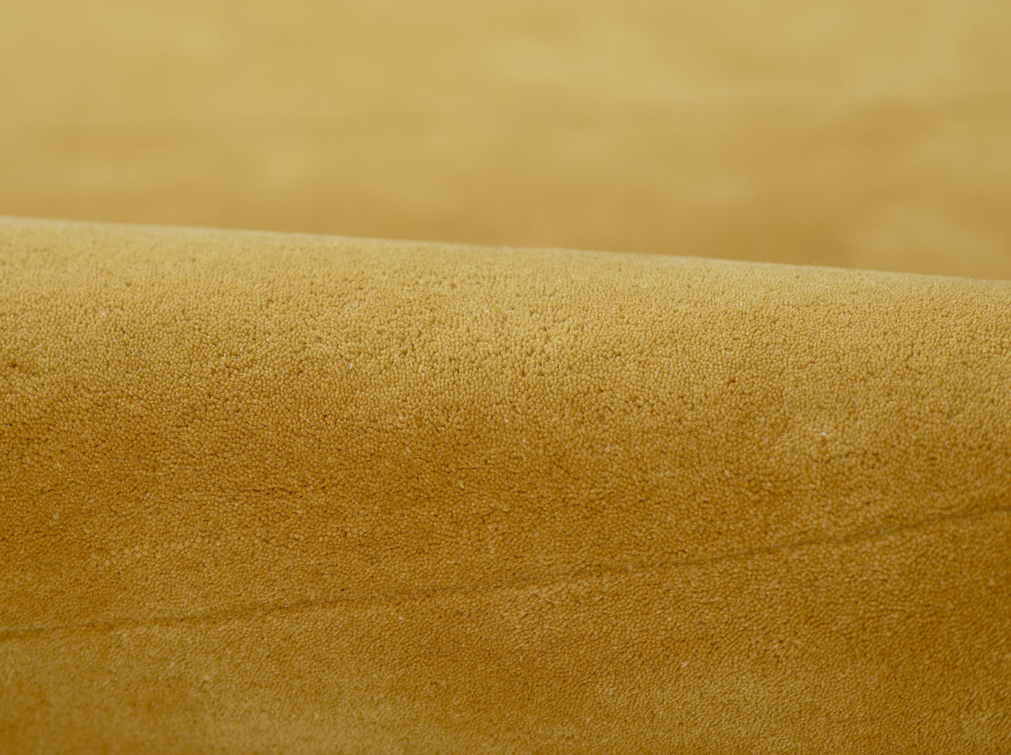 Golden tan suede close-up with soft nap and curved fold, a textured leather-like material.
