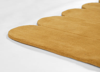 Beige suede-like rug with a rounded scalloped edge.