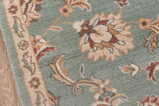 Teal floral rug with beige and cream flowers, pink accents, ornate border, wooden floor edge.