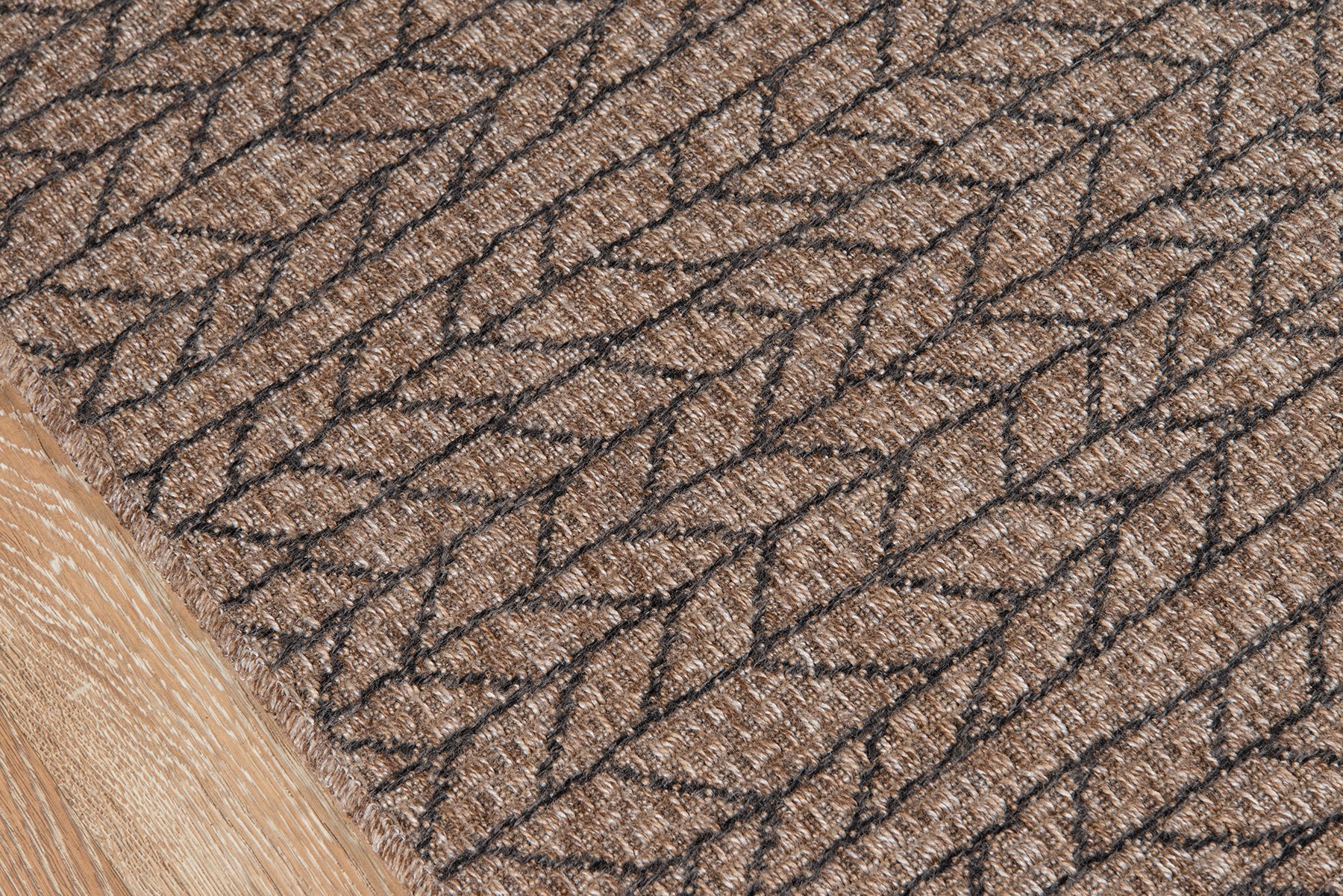 Close-up of tan woven rug with dark brown braided chain-like pattern on natural fibers.