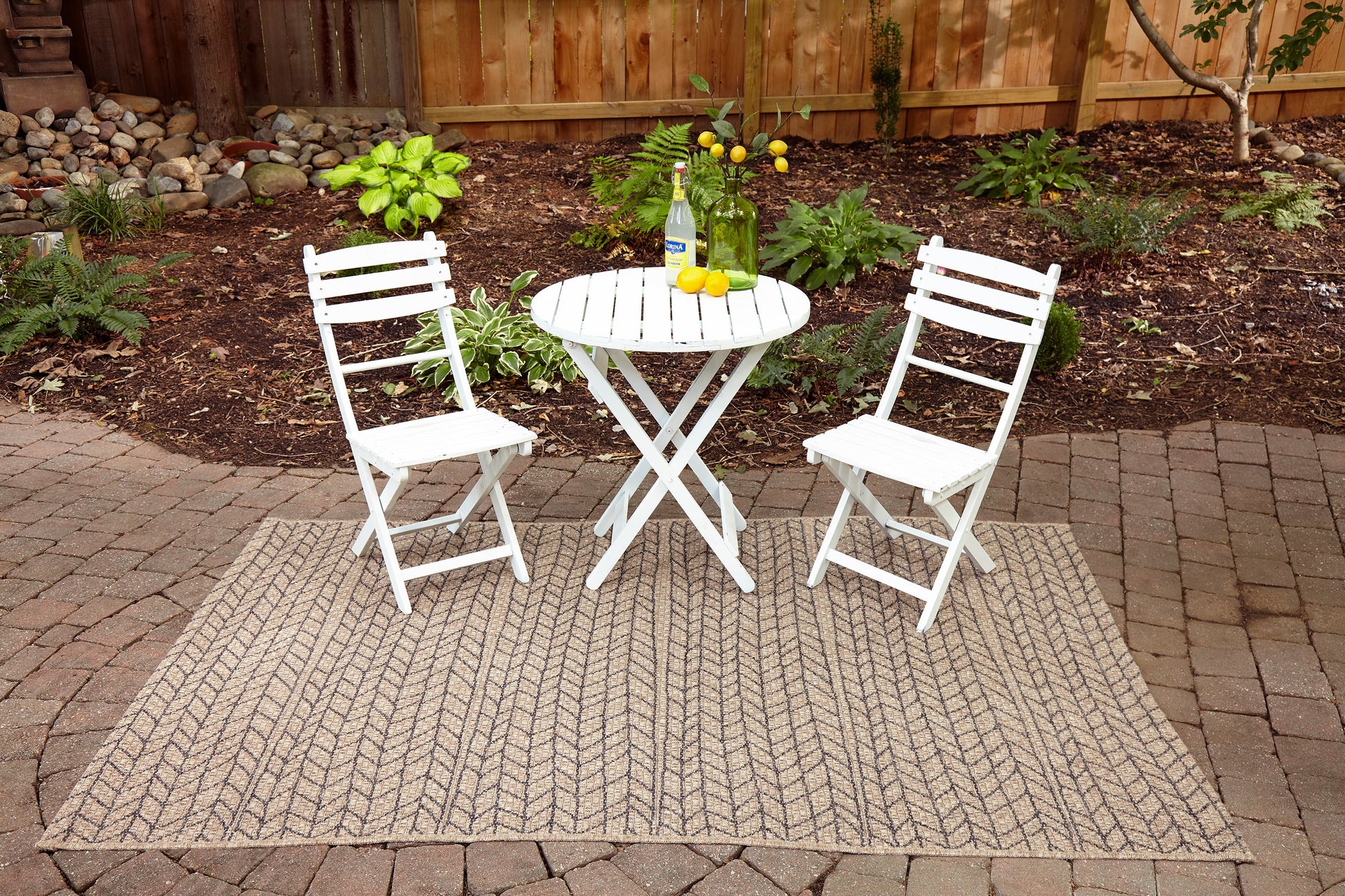 Tan chevron-pattern outdoor rug, 7' x 10', on a garden patio.