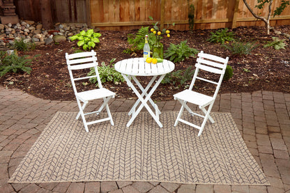 Tan woven outdoor rug, 10' x 13', laid in a garden.