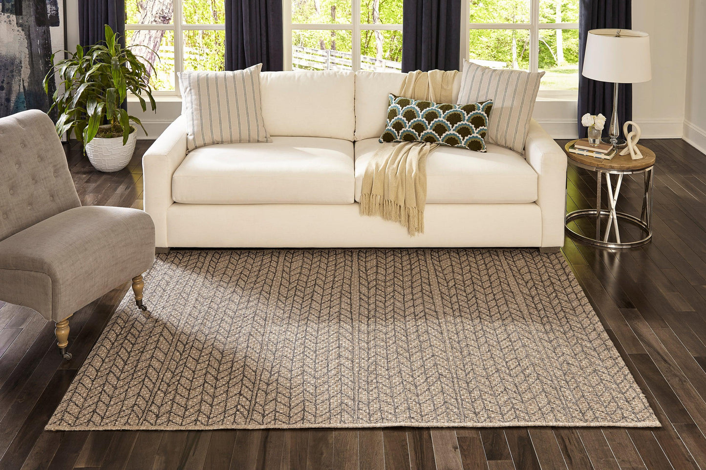 Tan area rug on dark wood floor, white sofa with striped pillows, throw blanket, gray accent chair, side table lamp.