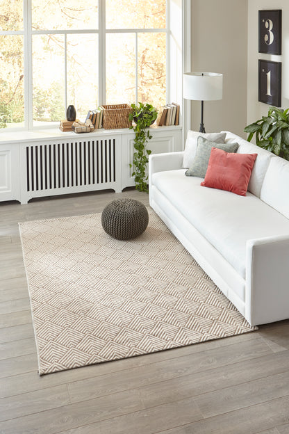 Bright modern living room with large windows, white sofa with coral cushion, beige chevron rug, round dark pouf and greenery