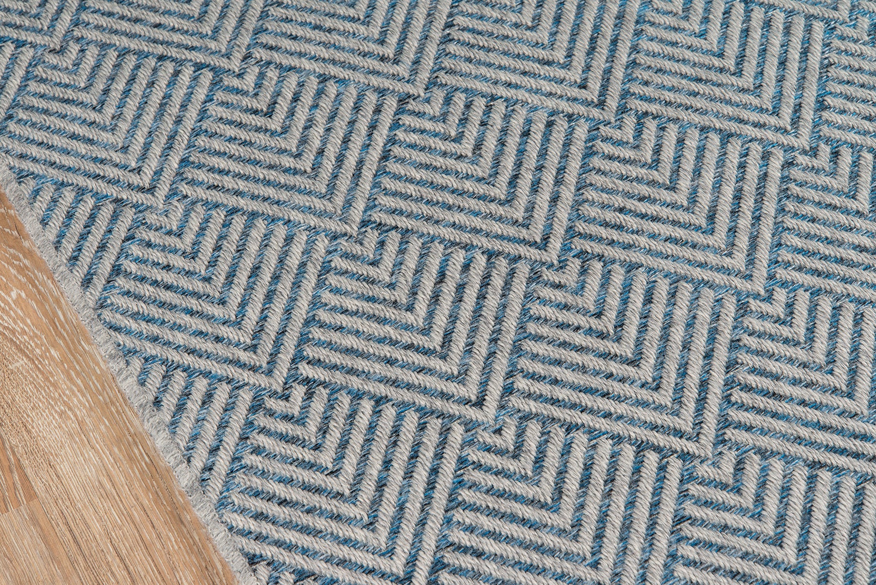 Blue woven rug with an interlocking square geometric pattern and a textured surface on a wooden floor.