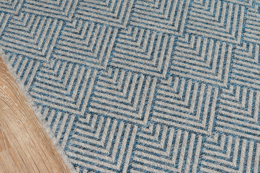 Blue geometric woven rug with beige interlocking square pattern; textured low-pile on wood floor.