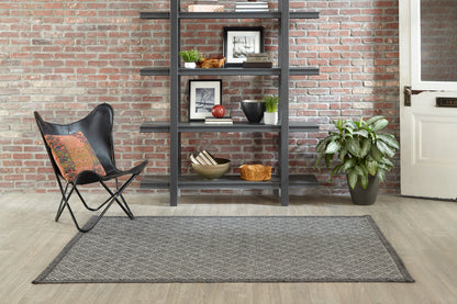 Rectangular gray woven rug on light wood floor, black butterfly chair with orange cushion, brick wall and shelving.