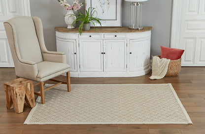 Tan woven runner rug on wood floor with cream tufted armchair and curved white distressed sideboard; plant, lamp, and blanket basket.