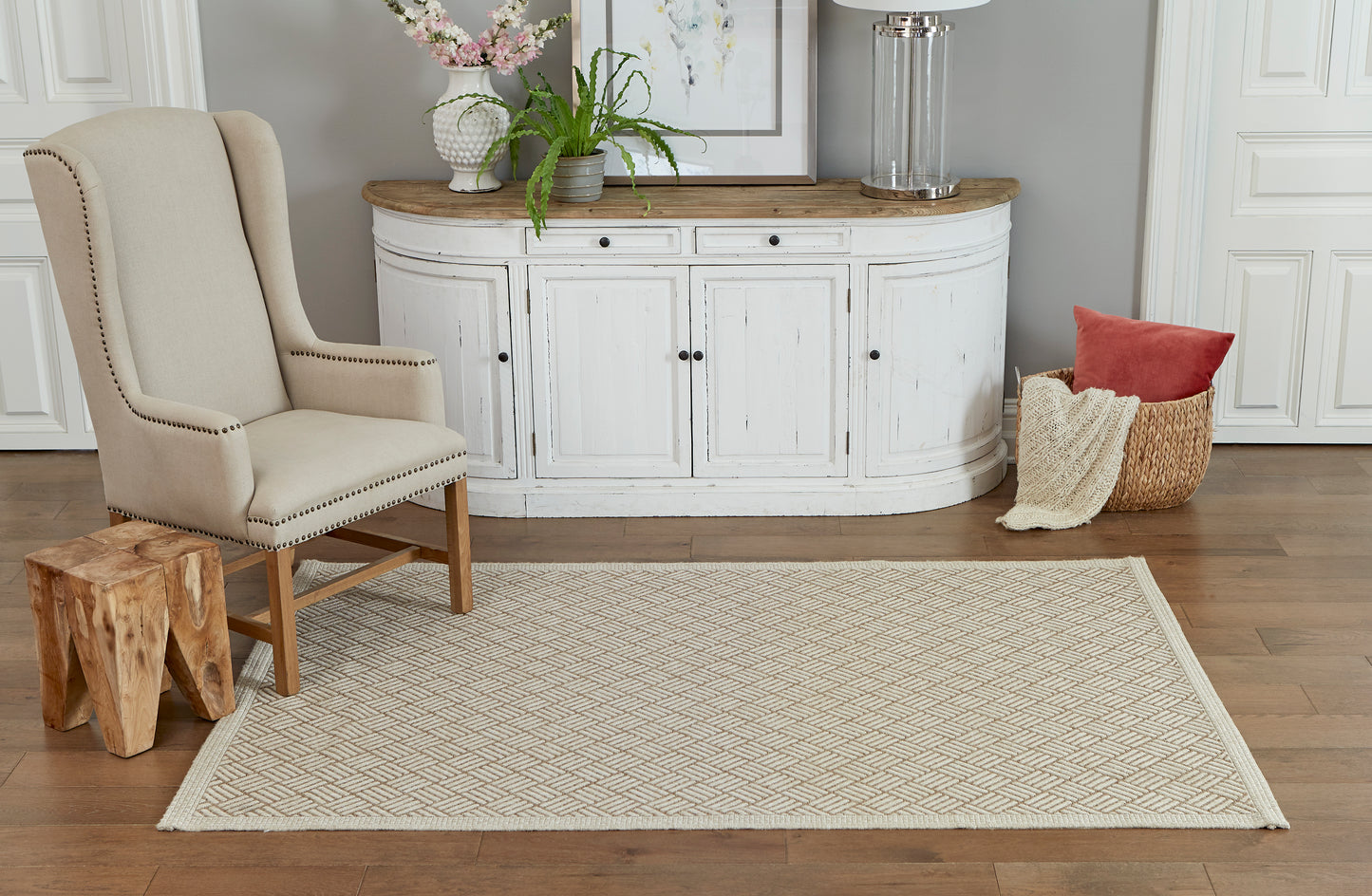 Tan rectangular woven area rug with subtle geometric pattern on hardwood floor in a coastal-style living room.