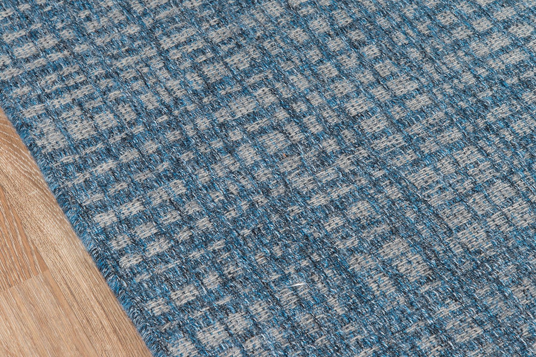 Blue textured woven rug with a subtle square pattern on a wooden floor.