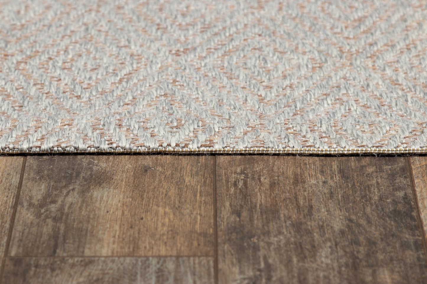 Gray geometric woven rug with a diamond pattern on dark brown wood floor.