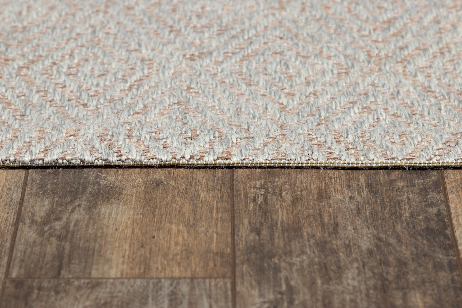 Gray geometric woven rug with a diamond pattern on dark brown wood floor.