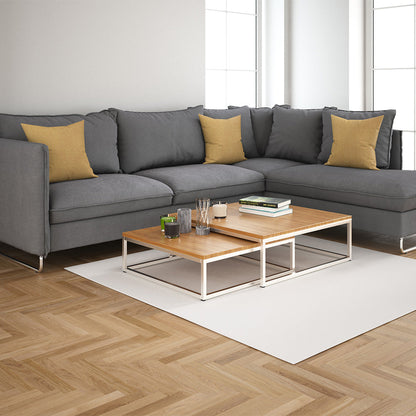 Gray sectional sofa with yellow throw pillows, two wood-topped nesting coffee tables on a white rug in a bright living room.