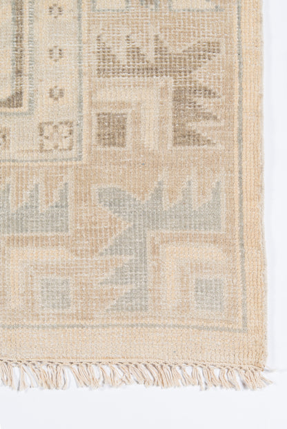 Beige woven area rug with geometric block motifs, pale blue-grey accents, and tassel fringe along the edge.