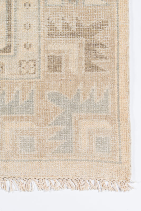 Beige woven rug with light blue-gray geometric motifs and fringed edge; kilim-style decorative floor rug.